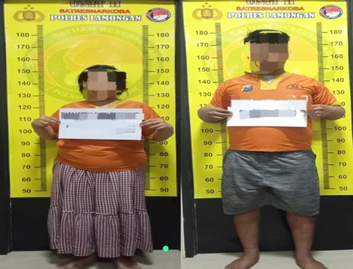 Dua tersangka berdiri di depan pengukur tinggi badan di Satresnarkoba Polres Lamongan